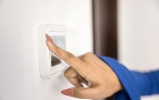 close up image of a hand pressing a button on a thermostat